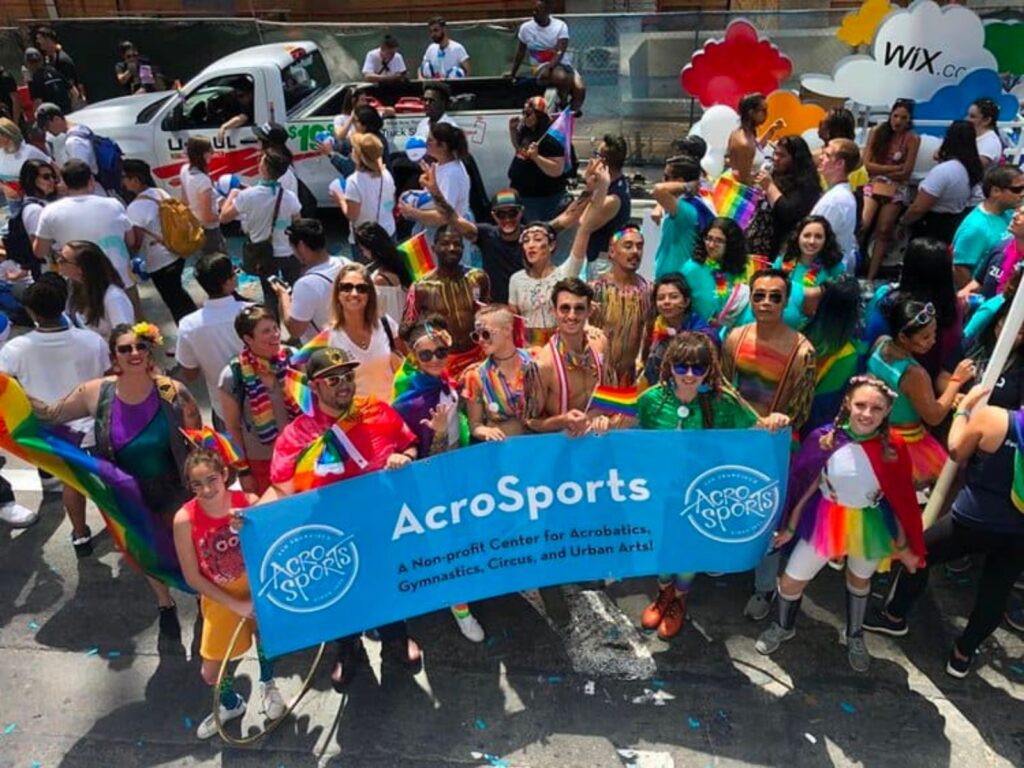 a group of people holding an AcroSports Banner and a rainbow flag in a parade