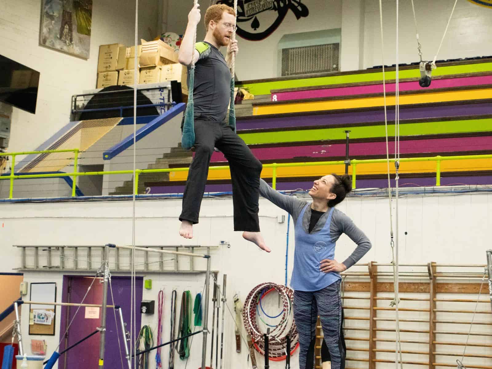 An instructor teaching an adult student how to trapeze at the AcroSports indoor gym in San Francisco.